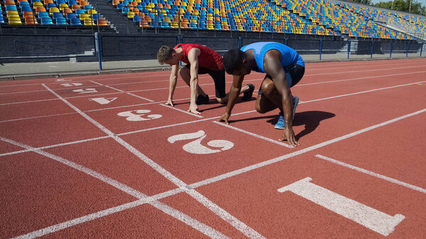Два мультирасовых спортсмена в стартовой позиции, готовых бежать после команды
