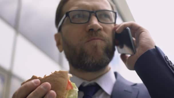 Nezdravá výživa, zaneprázdněný podnikatel mluví o telefonu a jíst hamburger oběd