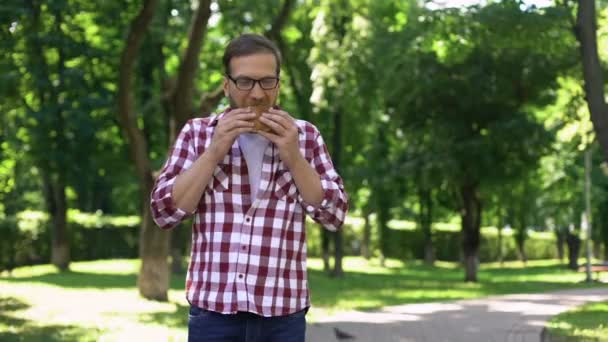 公園吐き気 食中毒症状のファーストフードのハンバーガーを噛む男 — ストック動画