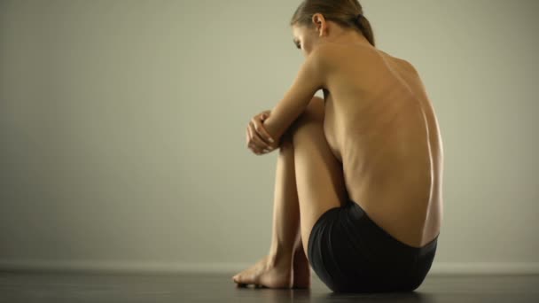 schlankes Mädchen mit Prellungen am Rücken auf dem Boden sitzend, häusliche Gewalt, wehrlos