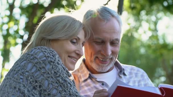 Äldre Par Titta Familjealbum Som Sitter Bänken Mysiga Trädgård Nostalgi — Stockvideo