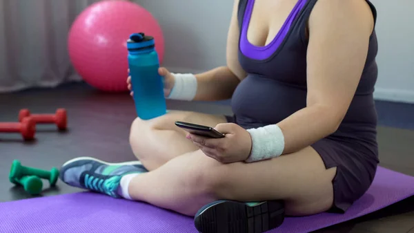 Obese lady scrolling sport app on her smartphone, watching weight loss results