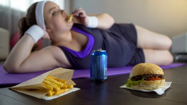 脂肪懒女孩在运动服吃垃圾食品 而不是训练瑜伽垫 — 图库照片