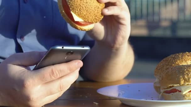 Hombre Con Sobrepeso Desplazándose Teléfono Inteligente Comer Hamburguesa Comida Rápida — Vídeos de Stock