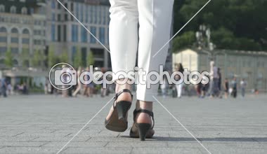 Kadın bacaklar beyaz pantolon ve şehir asfaltta, rahat Ayakkabı yürüyüş sandalet