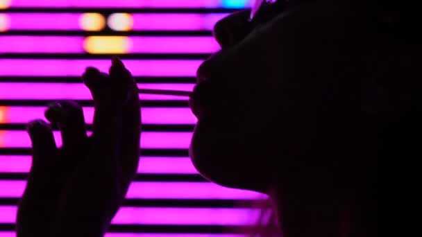 キャンディを舐めている ナイトクラブ ショーの照明でリラックスできる魅力的な女性 — ストック動画