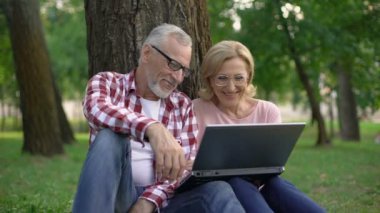 Mutlu emekli adam ve çim üzerinde oturan ve dizüstü pc film izlerken kadın
