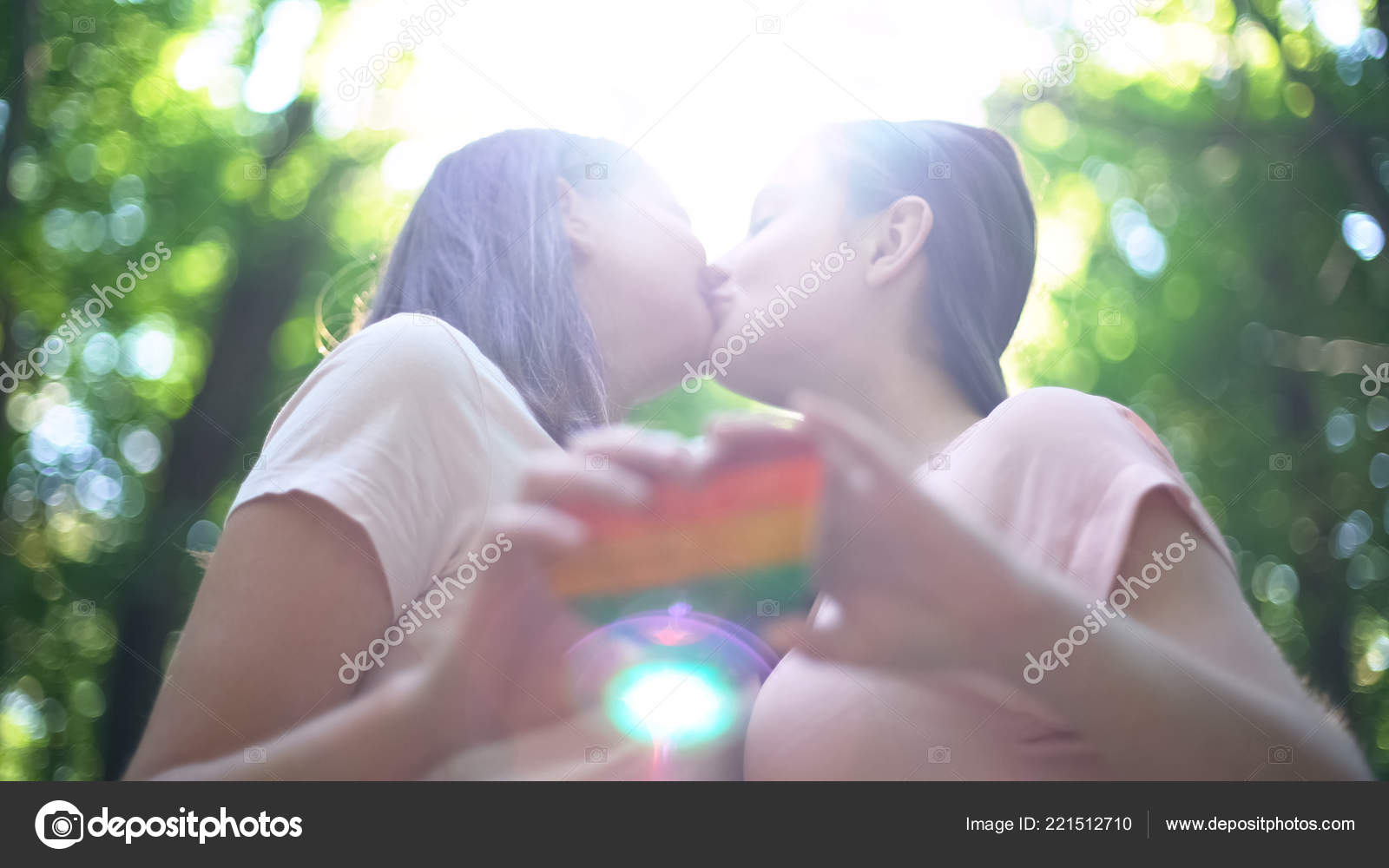 愉快的女同性恋情侣在爱接吻持有彩虹心脏Lgbt 骄傲旗— 图库照片©motortion＃221512710