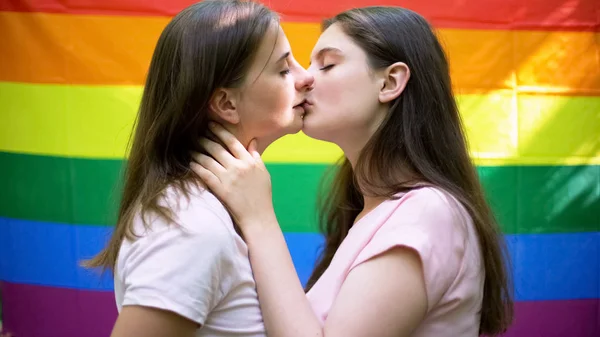 Lesbian couple kissing on rainbow flag background, same-sex relationship, l...