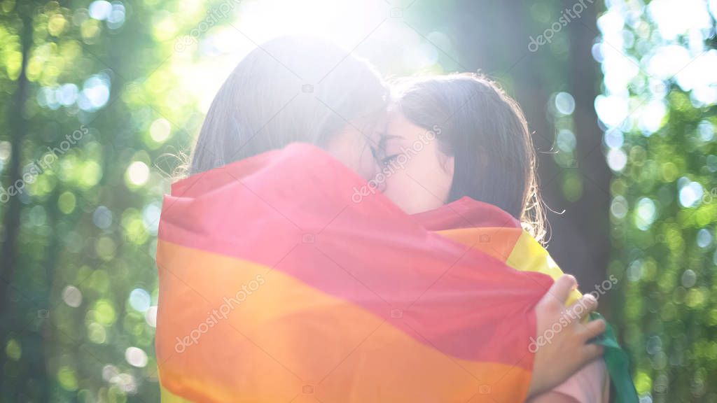 Lesbian lovers wrapped in rainbow flag kissing, tenderness and love, lgbt rights