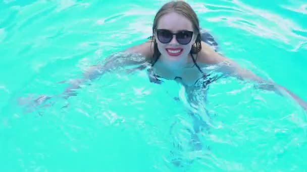 澄んだプールの水泳を楽しむスタイリッシュなサングラスのきれいな女性 — ストック動画