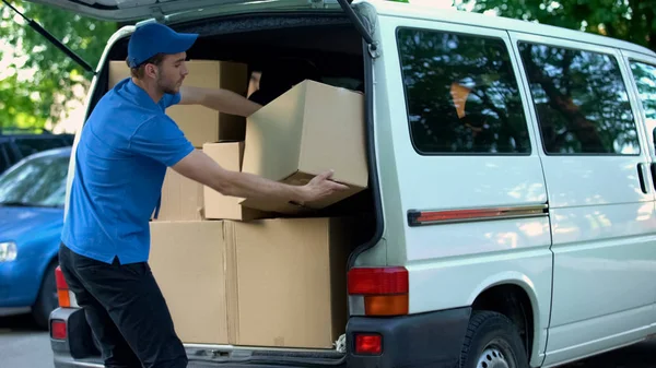 Male courier taking delivery boxes out from van, moving company, goods shipment