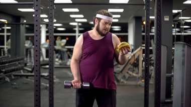 Overweight man holding burger and dumbbell in hands, life decision, motivation clipart