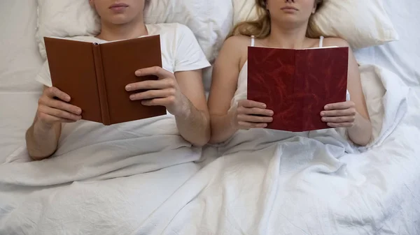 Young couple reading books in bed ignoring each other, intimate problem, rest