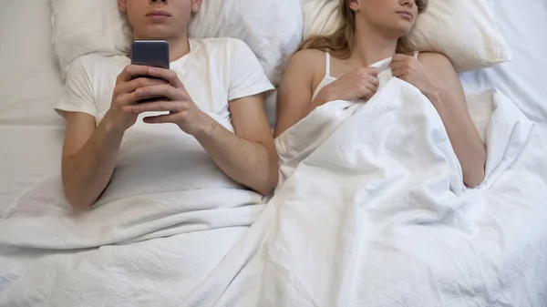 Boyfriend playing smartphone games in bed, ignoring girlfriend, couple problem