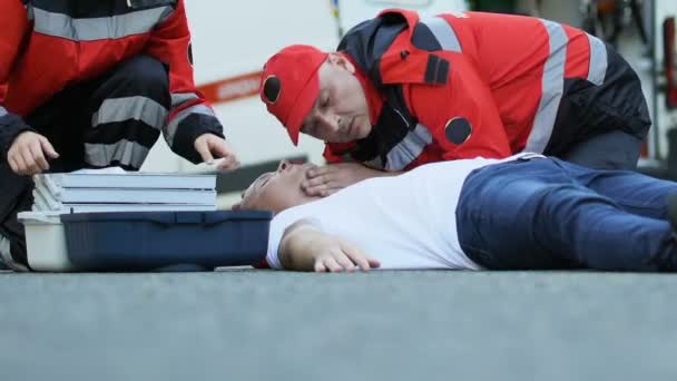 Команда Скорой Помощи Спасает Пациента Мужчину Лежащего Дороге Доктор Устанавливает — стоковое видео