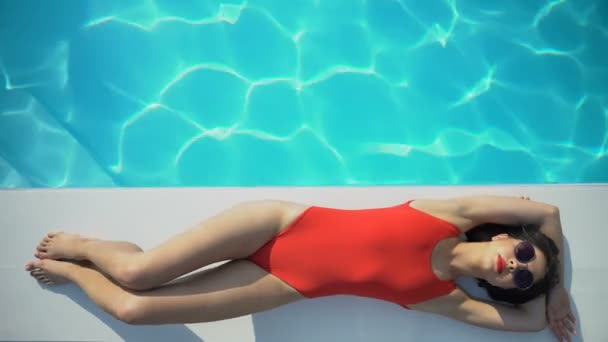 适合红色泳衣的女人在阳光明媚的日子里放松和躺在池畔 顶视图 — 图库视频影像