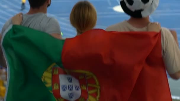 興奮したファンがジャンプし スタジアムでサッカーを見ているポルトガルの旗に包まれて — ストック動画
