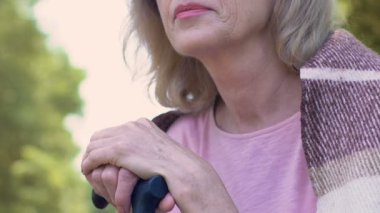 Mutsuz yaşlı kadın parkta bankta oturmuş ve baston, yalnızlık yaslanmış