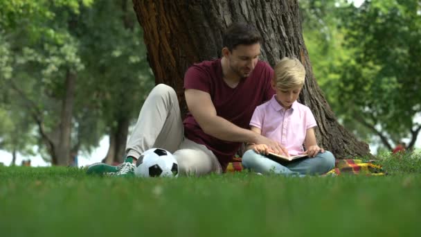 Padre Figlio Leggendo Libro Nel Parco Uomo Incoraggia Ragazzo Conoscere — Video Stock