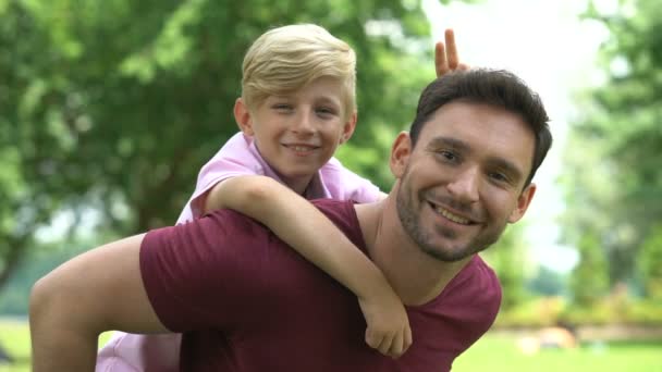 お父さんと息子のおんぶ 公園で週末休んで家族幸せな子供時代 — ストック動画