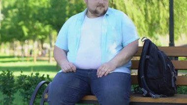 Komik tombul erkek parkta bankta oturan ve merakla geçenler seyir