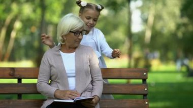 Sarılma ve öpüşme onu Büyükanne Park, kitap okumak için çalışan küçük kız