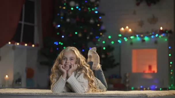 輝くクリスマス ツリー 居心地の良い暖炉の祭典の近くの床に横たわった少女 — ストック動画