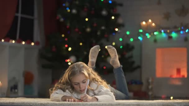 愛らしい少女の奇跡を夢見て光るクリスマス ツリーの下の手紙を書く — ストック動画