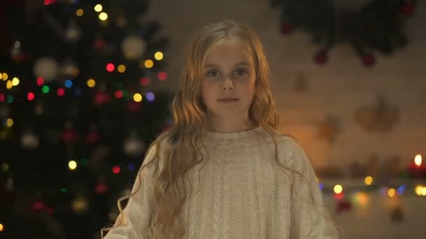 かわいい女の子の後ろに輝くクリスマス ツリー カメラを手でハートを作る — ストック動画