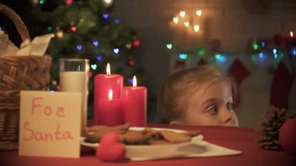 Menina sorridente olhando para fora sob a mesa e tomando gengibre tradicional biscoito X-mas — Vídeo de Stock