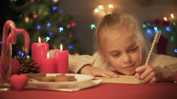 Linda chica escribiendo carta para Santa en la mesa decorada para Navidad, lista de deseos — Vídeos de Stock