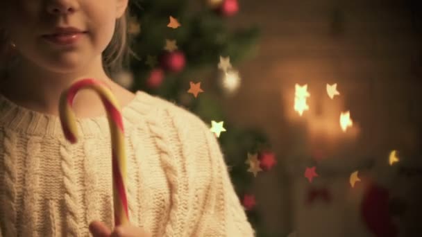 Niedliche Kind leckt traditionelle Weihnachtsbonbons lächelnd in die Kamera Dekorationen glühend — Stockvideo