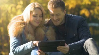 Mutlu çift tablet, alışveriş veya tur seçimi sonbahar parkta oturan kullanma