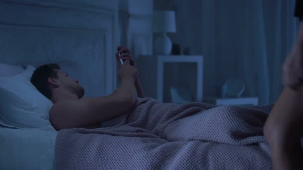 躺在床上的男人在智能手机上聊天 女友穿着诱人的内衣 — 图库视频影像