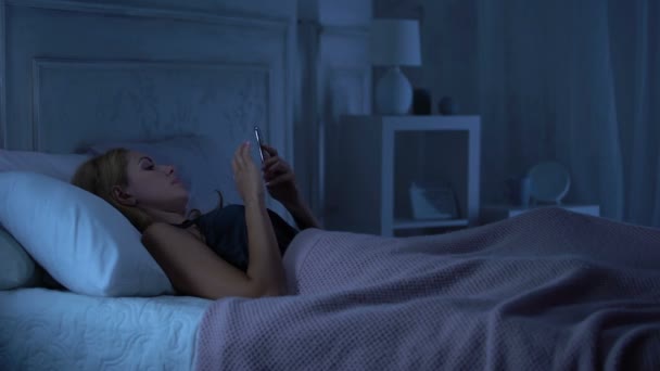 魅惑的なランジェリーを来て彼氏スマート フォンでチャットのベッドで横になっている女性 — ストック動画