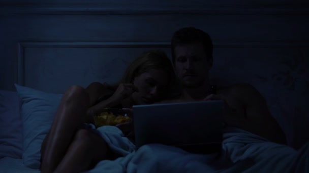 女性と暗い部屋でベッドの上に座って ノート パソコンでホラー映画を見ている男 — ストック動画