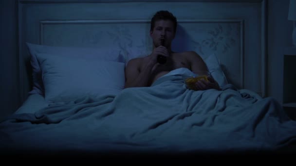 Pria Lajang Berbaring Tempat Tidur Menonton Acara Dan Makan Makanan — Stok Video