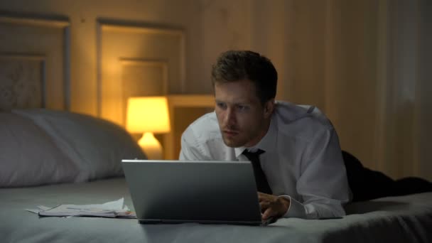 ベッドに横たわっている思いやりのある男性と ビジネス電子メールのラップトップ上で文書を読む — ストック動画