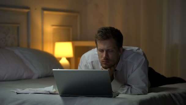 メールを読んで疲れエンジニア ノート パソコンで作業のベッドの上に横たわって ヨーイング — ストック動画