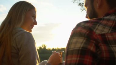 Girl drinking tea and flirting with bearded man, couple sitting near forest lake