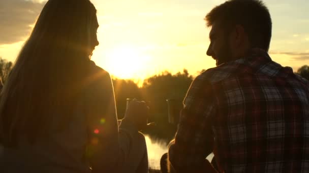 女性と男性 リバーサイドでお茶を飲んで美しい夕日を楽しむキャンプ — ストック動画