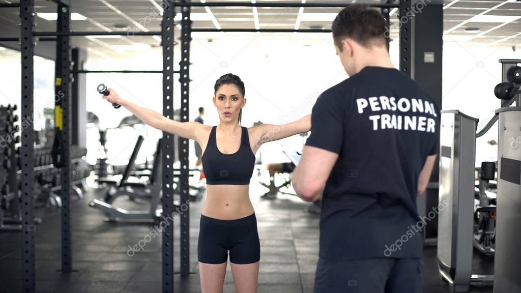 Active woman doing exercise with dumbbells during workout with personal trainer