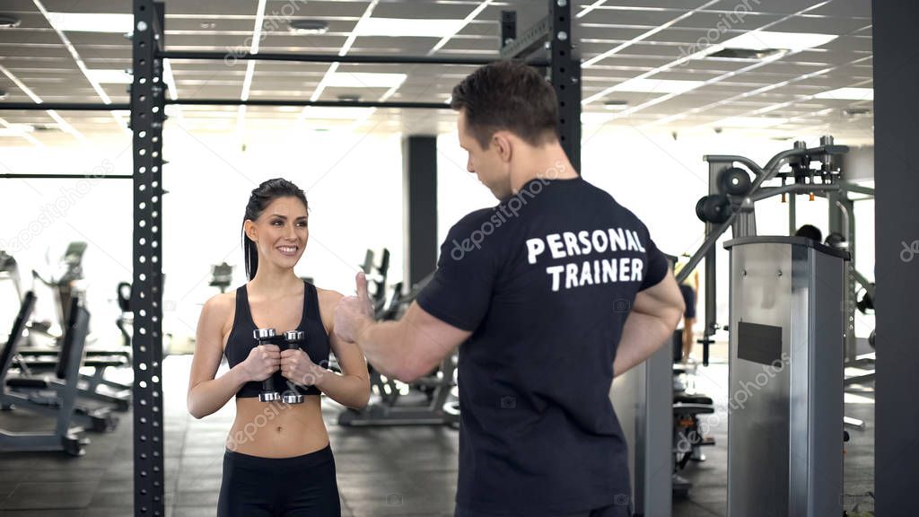Personal trainer showing thumbs up to fit girl while exercising, motivation