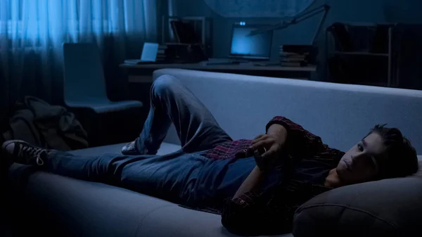 ティーンエイ ジャーの男の子ソファーで横になっている間 夜のテレビ番組を見て感じて退屈 — ストック写真