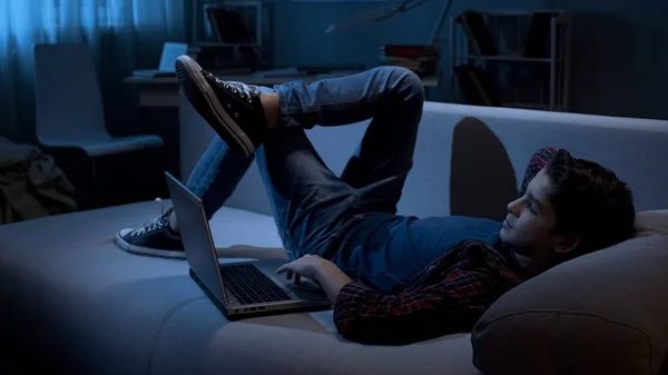 男性青少年沉溺于躺在沙发上的小工具和网上冲浪 笔记本电脑 — 图库照片