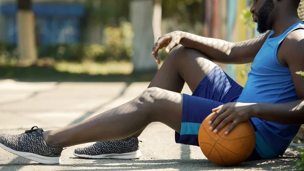 ボールを保持している 地面の上に座って動揺してアフリカ系アメリカ人のバスケット ボール選手 — ストック写真