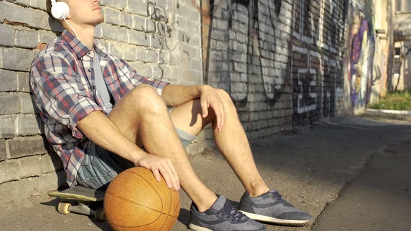 Aktiver Mann Sitzt Auf Skateboard Spielt Ball Und Hört Musik — Stockfoto