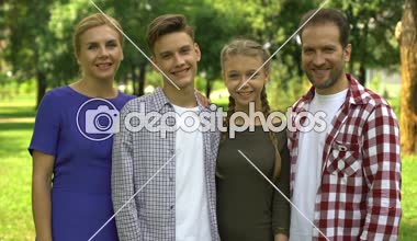 Parkta hafta sonu zevk ve kameraya başparmak gösterilmesini neşeli aile üyeleri