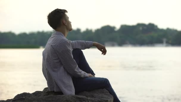 忧郁的男性少年独自坐在河边的石头上思考生活 — 图库视频影像